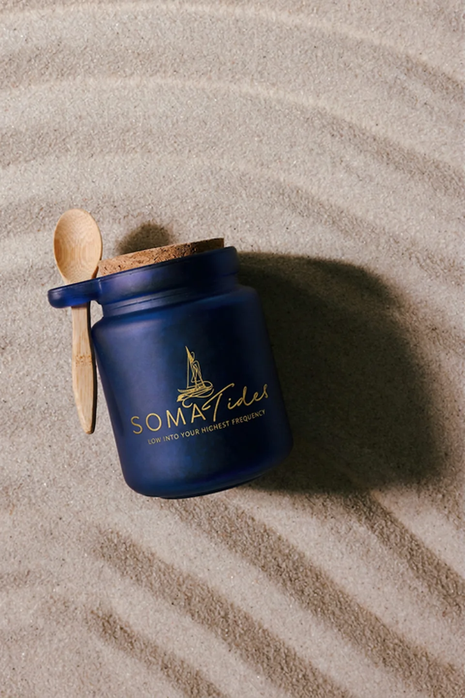 Soma Tides cork-lidded jar with a bamboo spoon resting on rippled sand